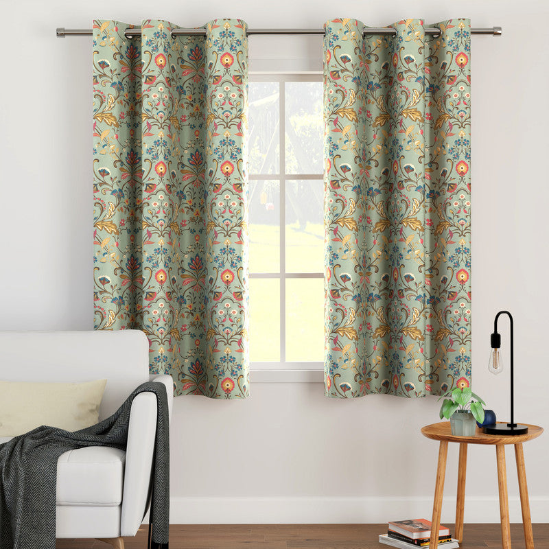 Sage floral print curtains hung on a plain steel rod at a living-room window, sofa and side lamp beside it