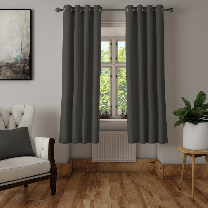 Solid charcoal grey curtains on steel eyelets against a pale grey wall, beside a cream armchair