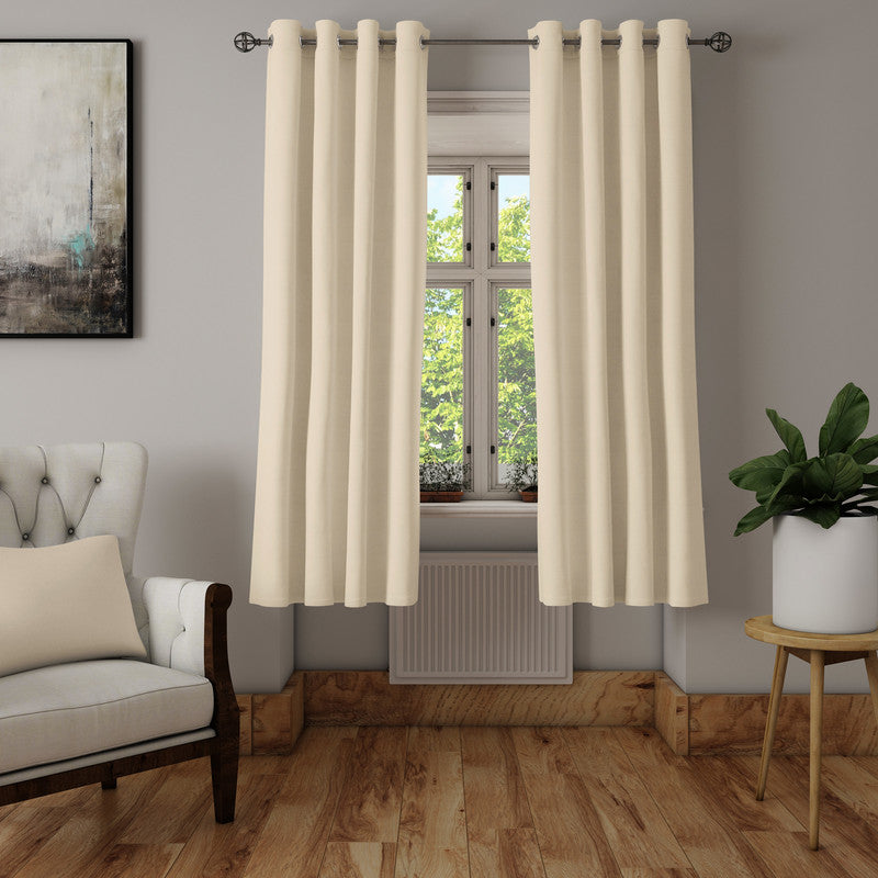Cream cotton curtains on silver eyelets at a bright window, with a cream armchair, a plant and a wooden floor