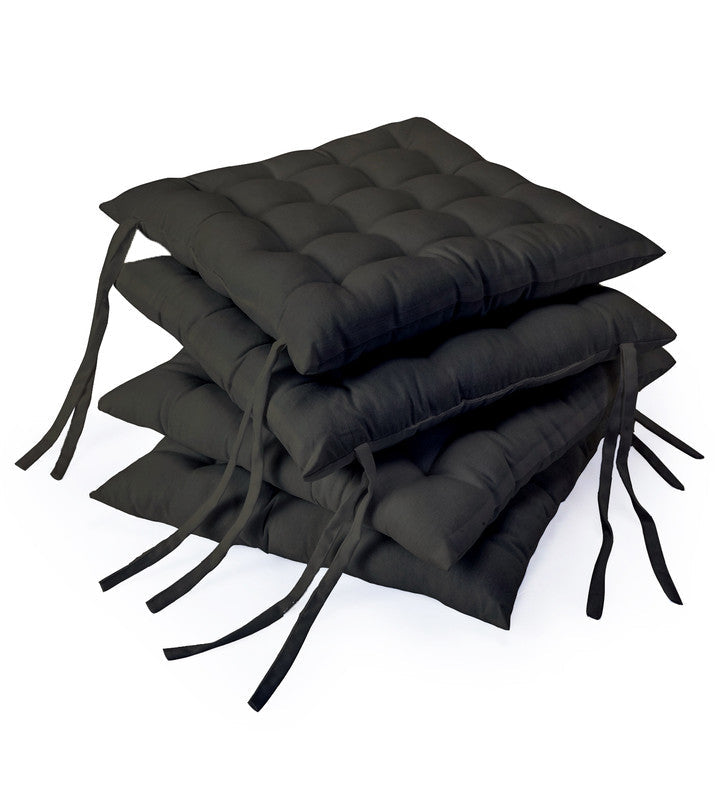 Four charcoal grey cotton chair pads stacked, showing the tufted top and the long fabric ties
