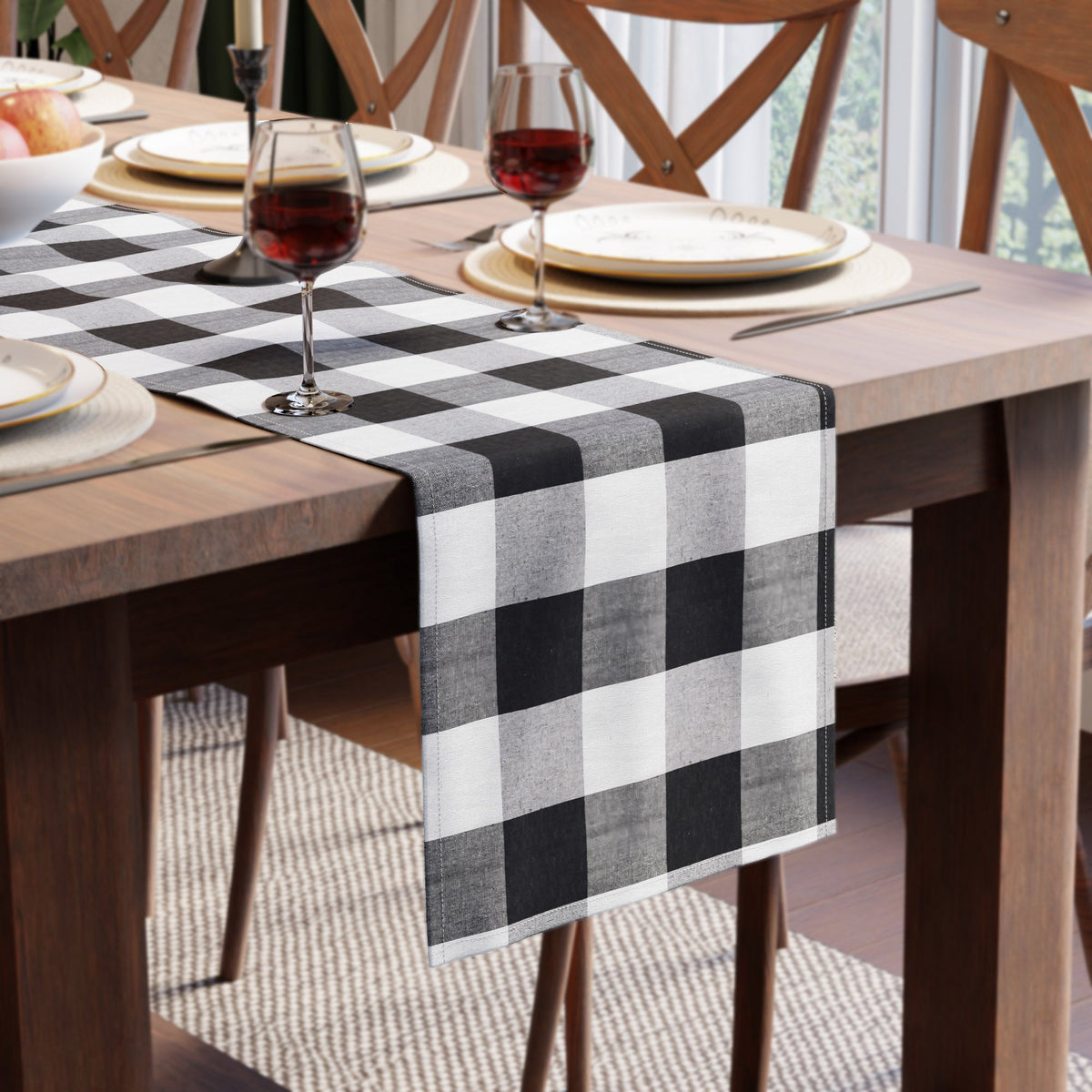 Black and white check cotton runner laid across a wooden dining table with plates, wine glasses and a bowl of apples