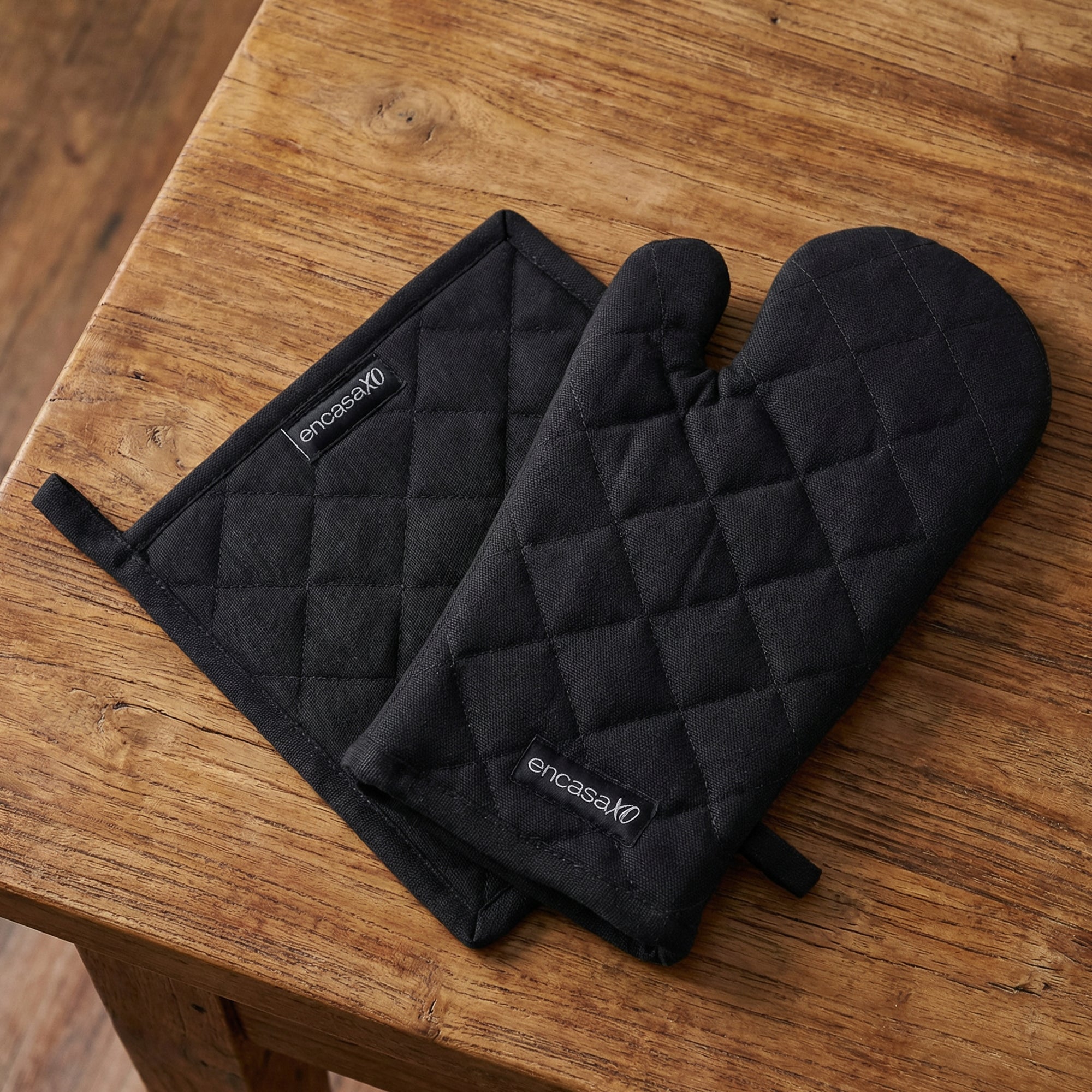 Black quilted cotton oven glove and matching pot holder laid on a wood table