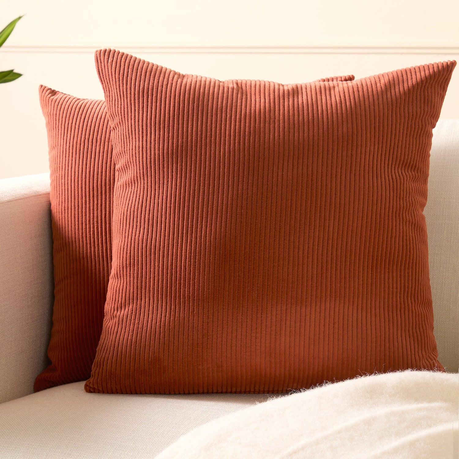 Two ribbed brick corduroy cushion covers resting on a cream sofa