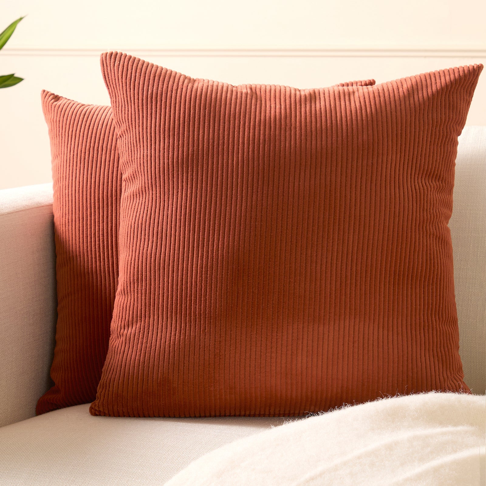 Two ribbed brick corduroy cushion covers resting on a cream sofa