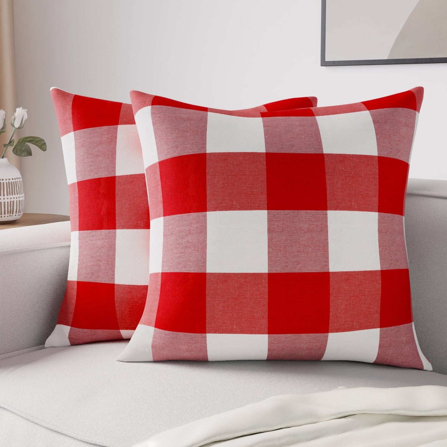 Red buffalo-check cushion covers styled on a white sofa with plant and wall art
