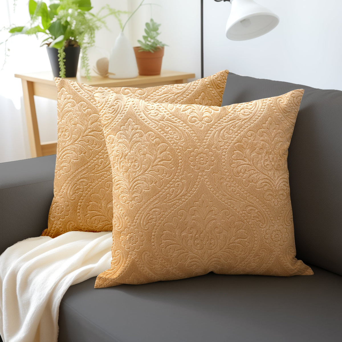 Two gold embossed velvet cushion covers with a damask pattern on a grey sofa beside a cream throw