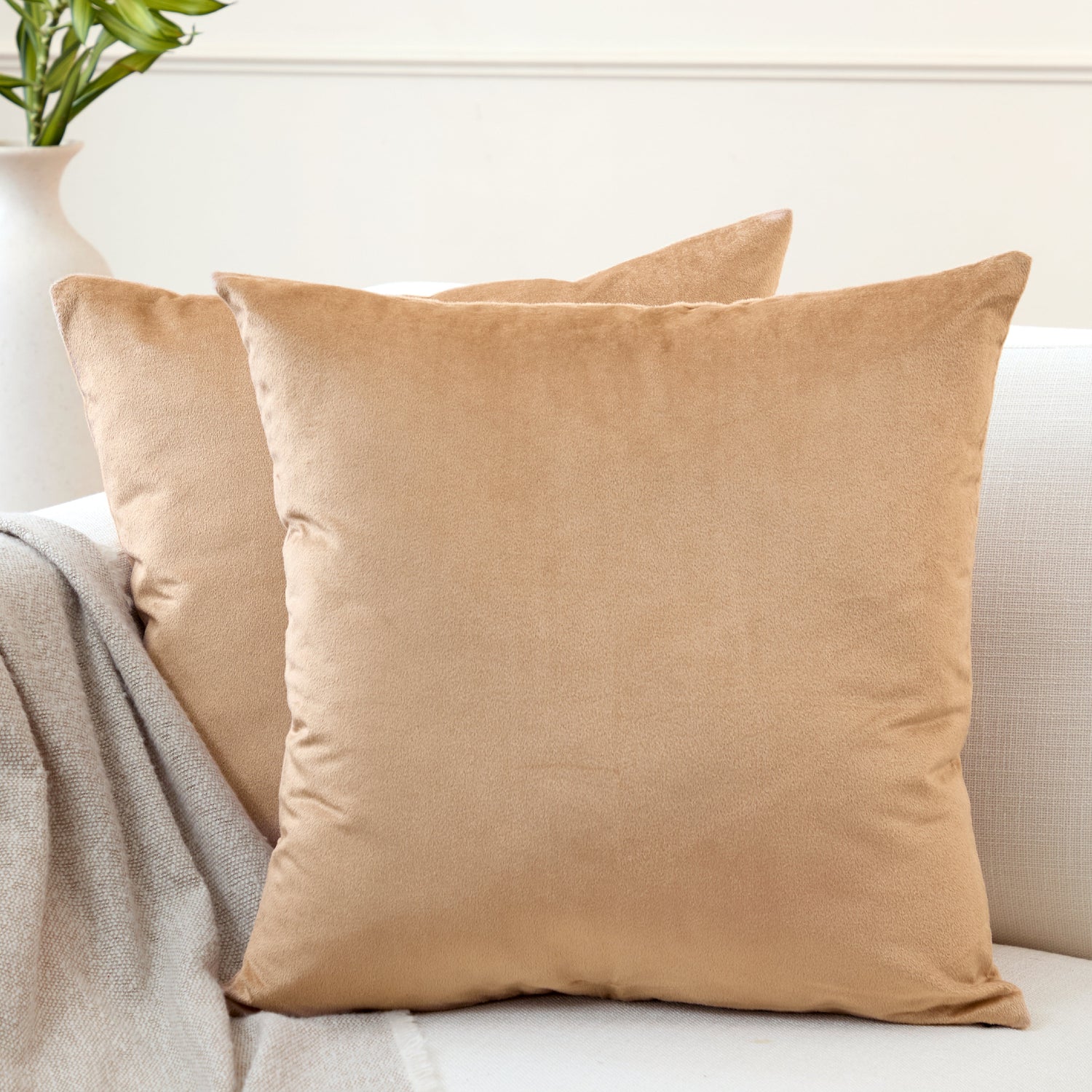 Two mustard gold velvet cushion covers stacked on the arm of a cream sofa with a grey knit throw