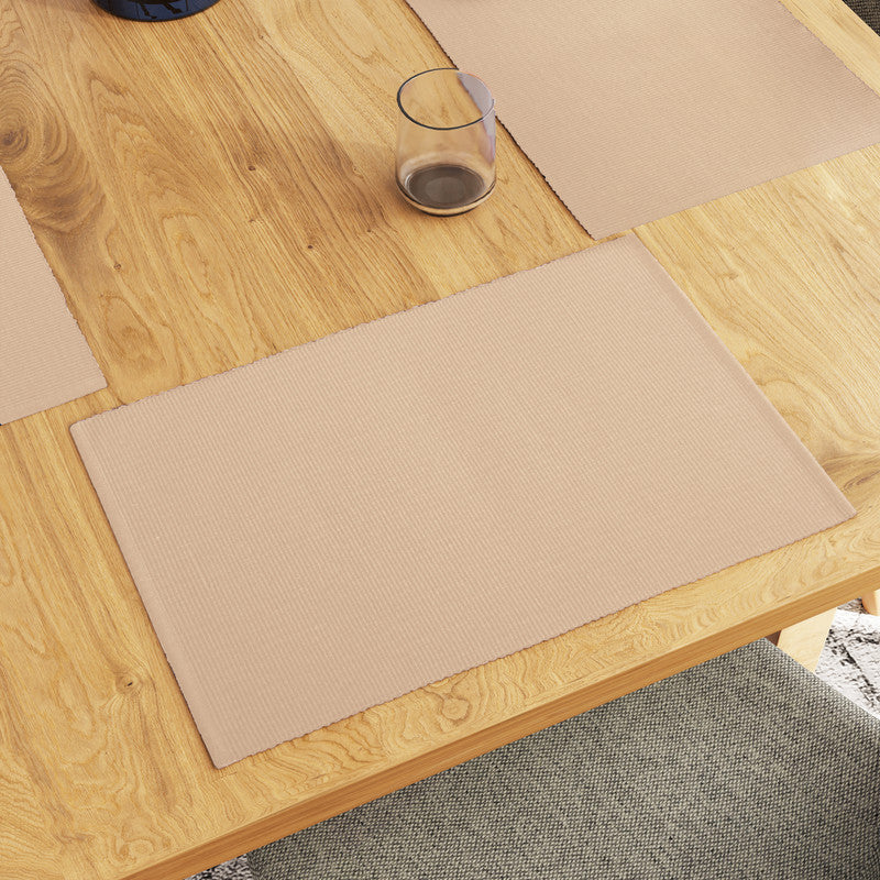 Beige ribbed cotton placemats laid on a wooden dining table with cutlery