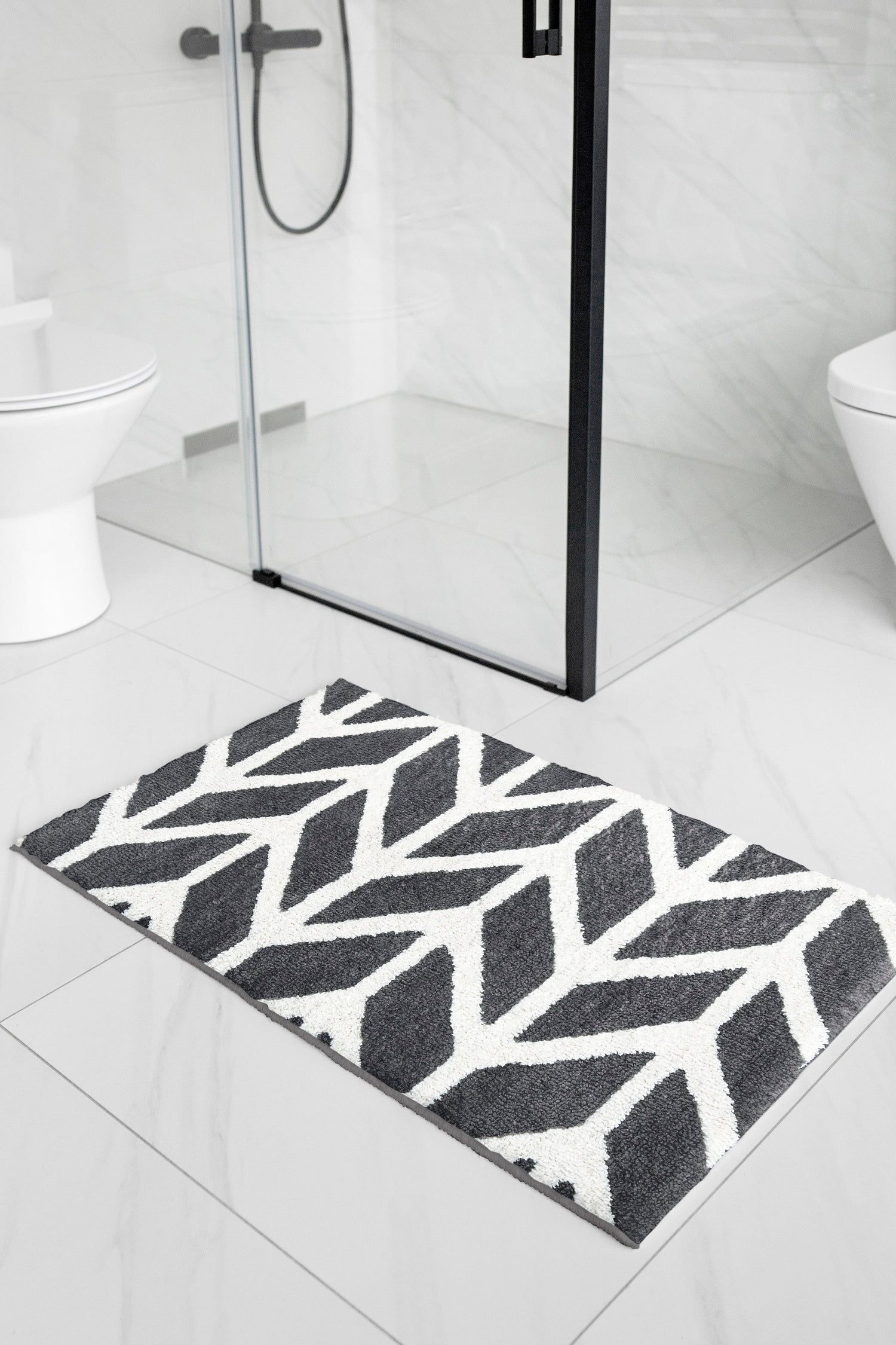 Dark grey and white patterned bath mat on white tile outside a glass shower cubicle