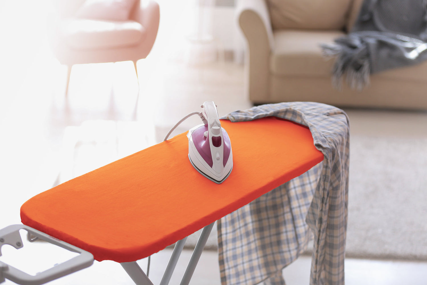Orange fitted ironing board cover on a board with an iron resting, in a bright room