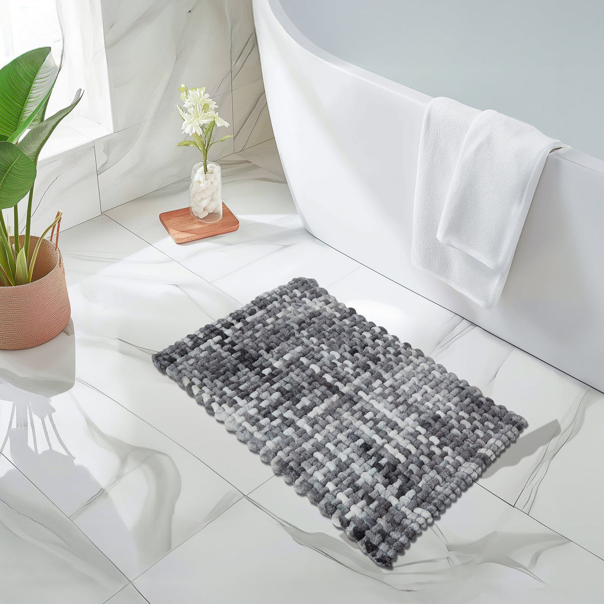 Grey and white loop-pile bath mat on white marble tiles beside a freestanding tub with a white towel over its rim