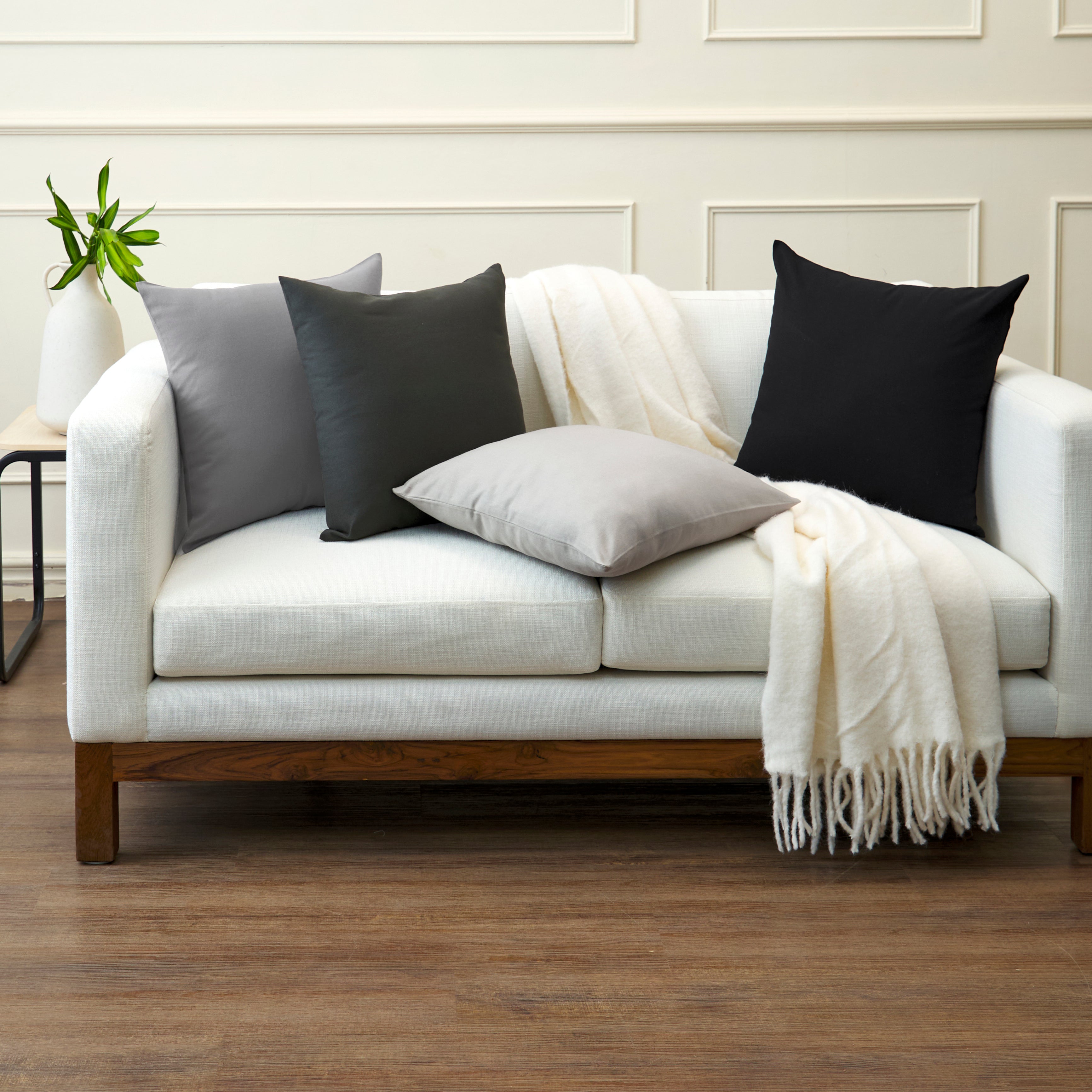 Grey, charcoal and black cushion covers layered at different heights on a white two-seater sofa
