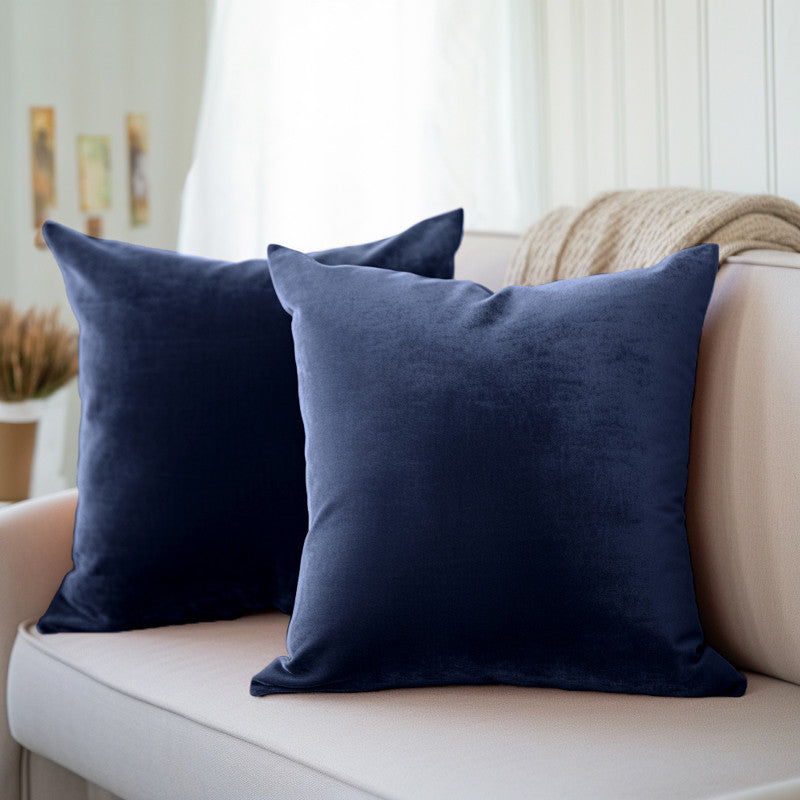 Two navy blue velvet cushion covers on a cream sofa beside a sheer curtain and a knit throw