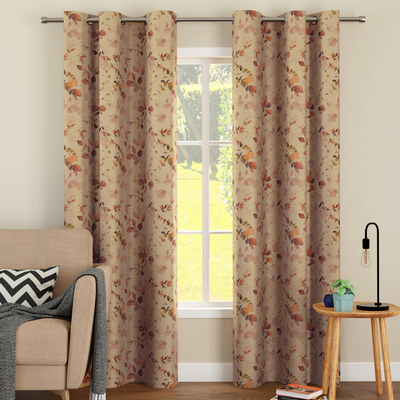 Cream curtains with a rust and brown leaf print hanging to the floor on steel eyelets beside a beige sofa