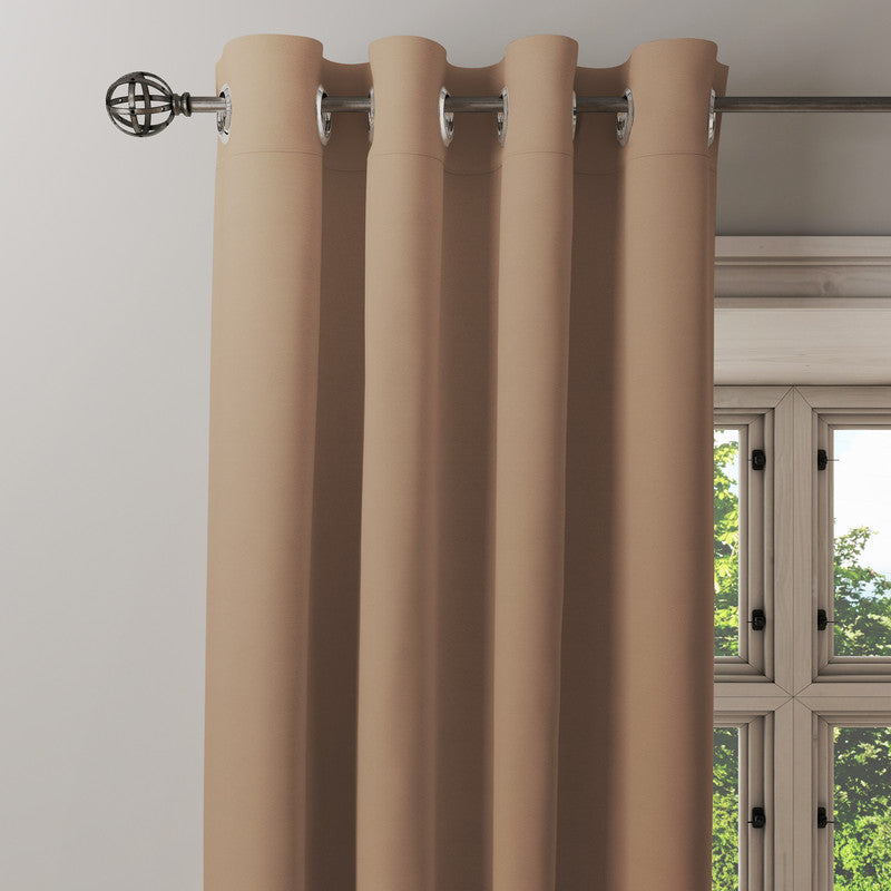 Plain beige cotton eyelet curtain hanging from a metal rod beside a window