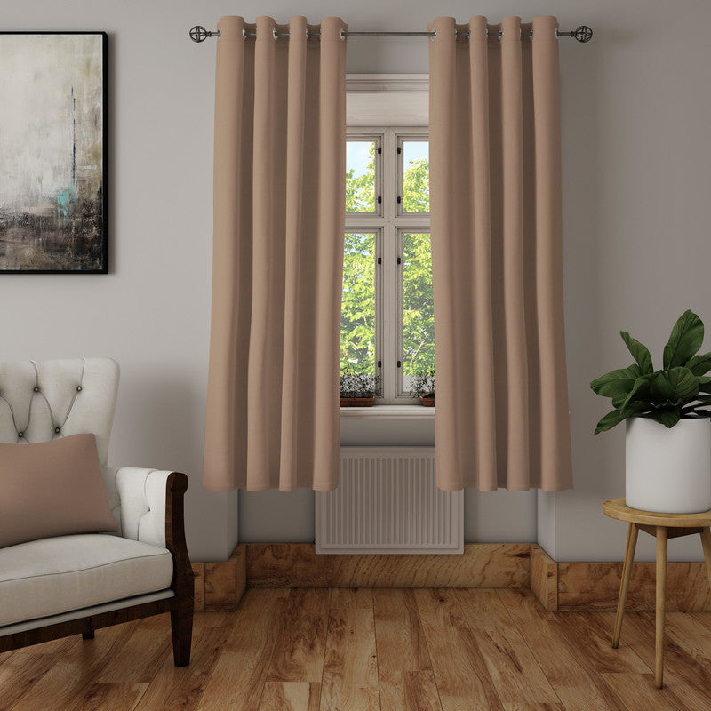 Warm beige eyelet curtains on a metal rod beside a cream tufted armchair, wood floor and a potted plant