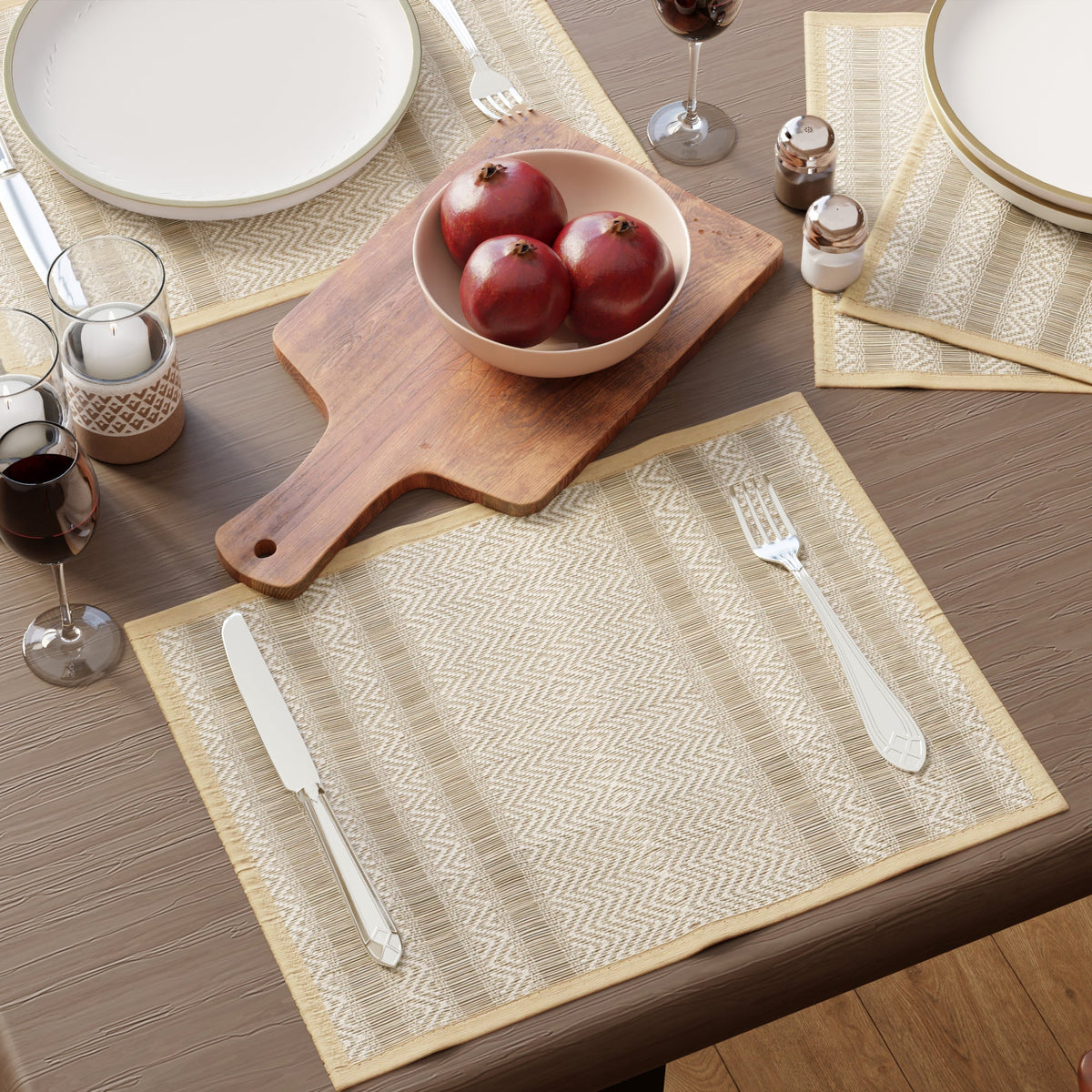 Handwoven beige grass table mats with cutlery, wine glasses and a bowl of pomegranates on a wooden table