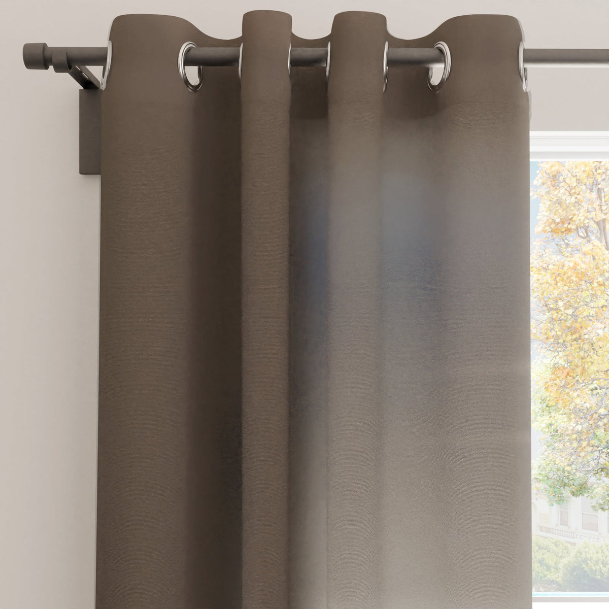 Taupe cotton canvas curtain panel hanging from a dark rod on silver eyelets beside a sunlit window
