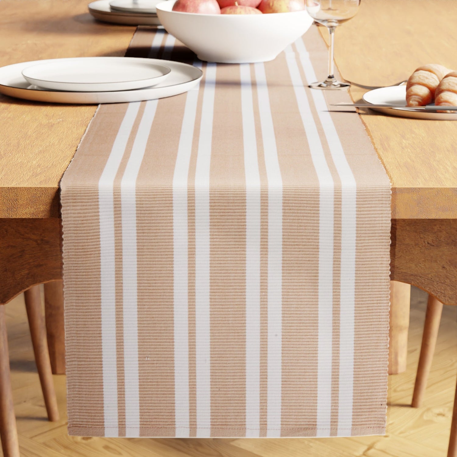 Beige striped cotton table runner down a wooden dining table set with plates