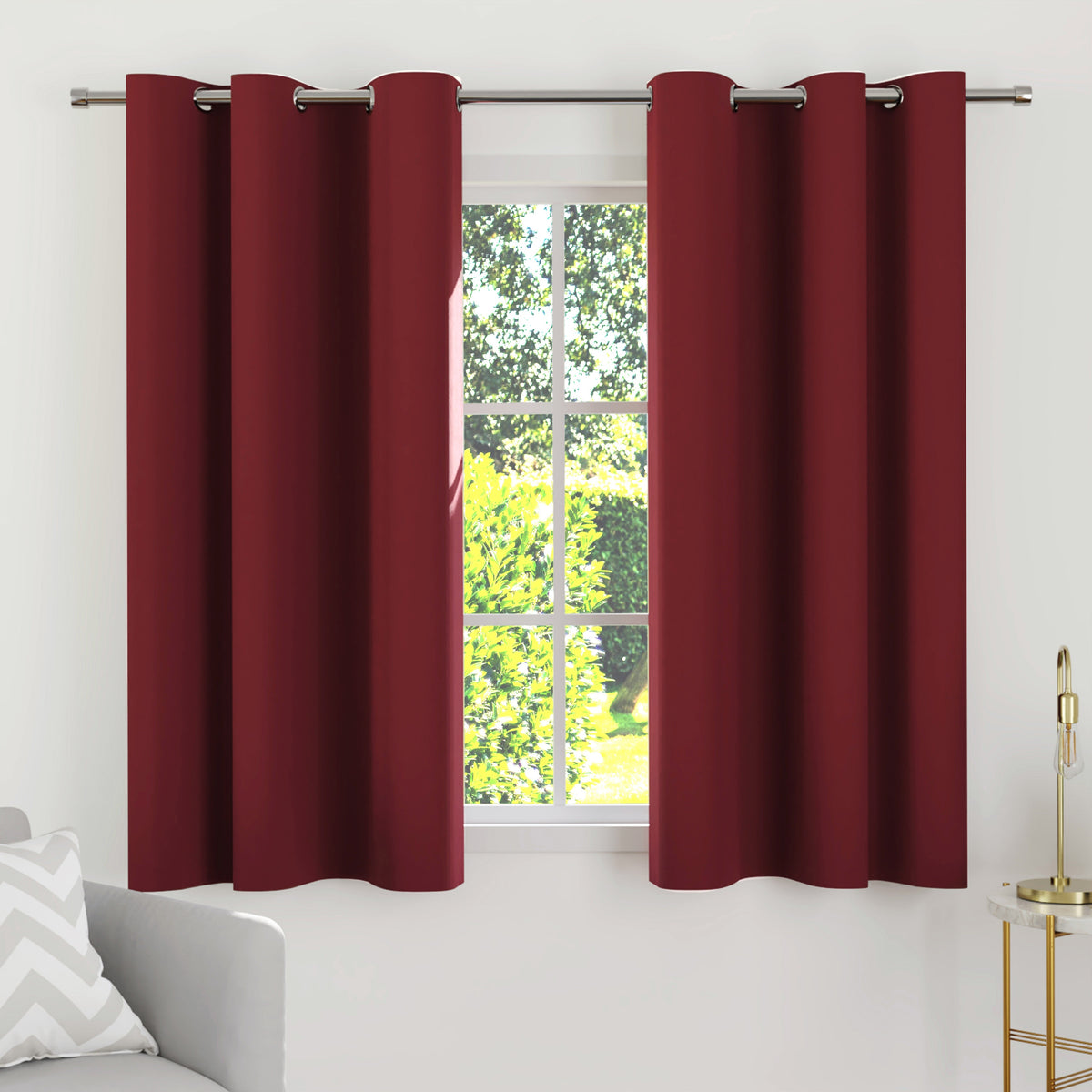Deep maroon blackout curtains on a steel rod at a white window, ending just below the sill