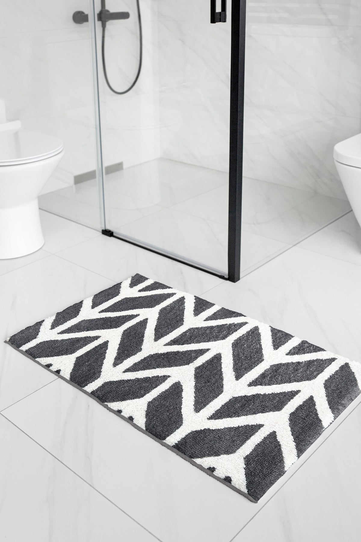 Dark grey and white patterned bath mat on white tile outside a glass shower cubicle