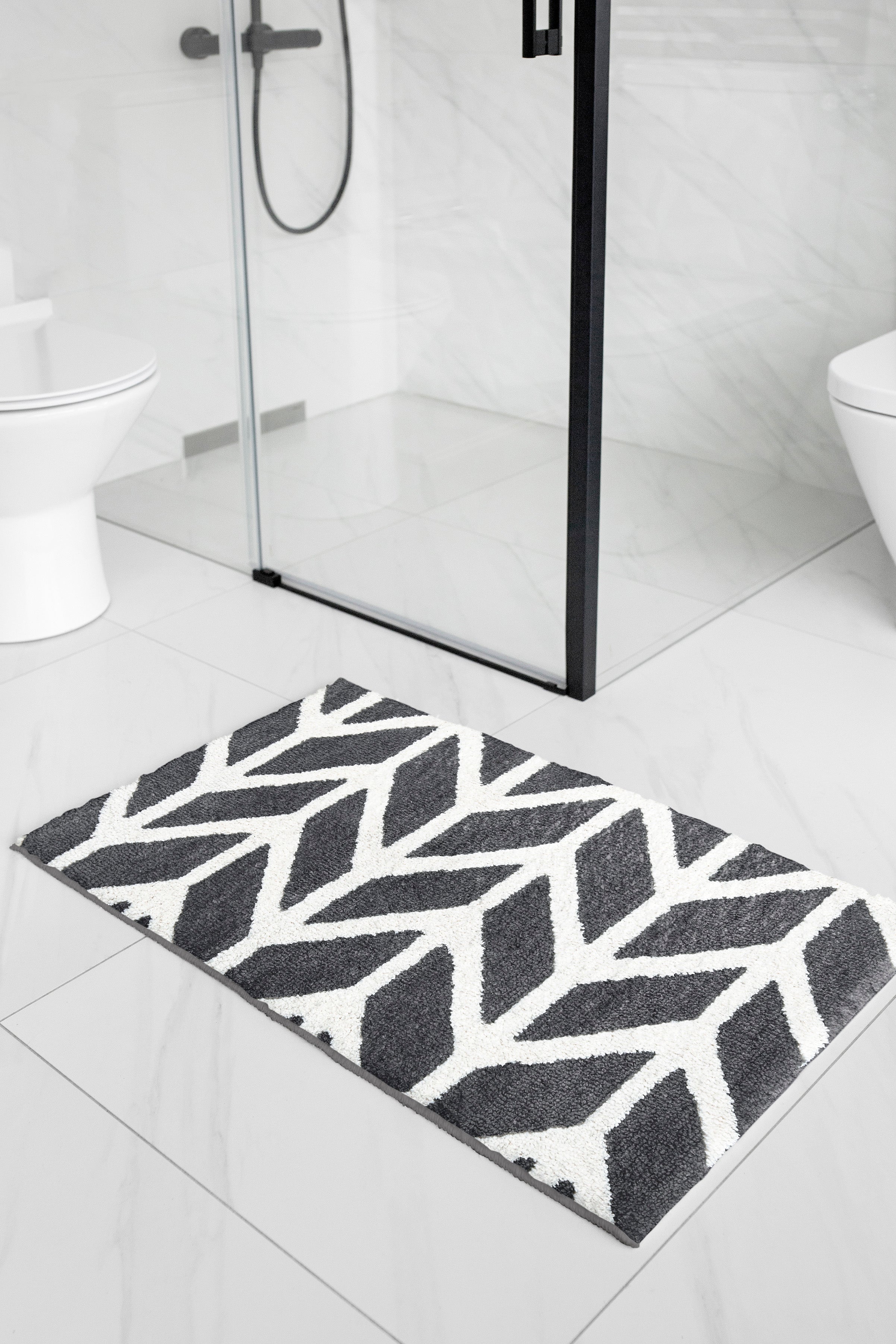 Dark grey and white patterned bath mat on white tile outside a glass shower cubicle
