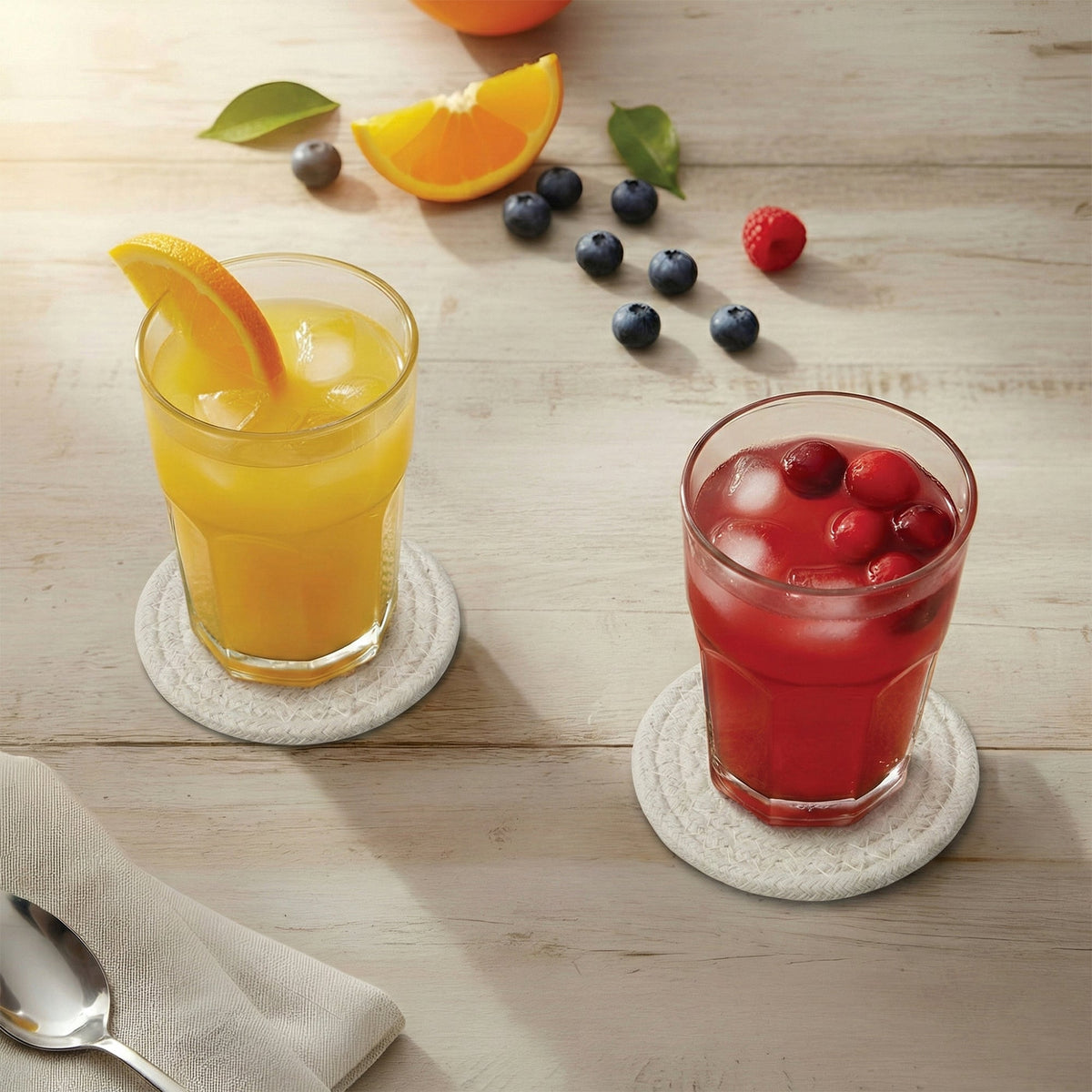 Orange juice and cranberry juice glasses on off-white cotton coasters on a pale whitewashed plank table