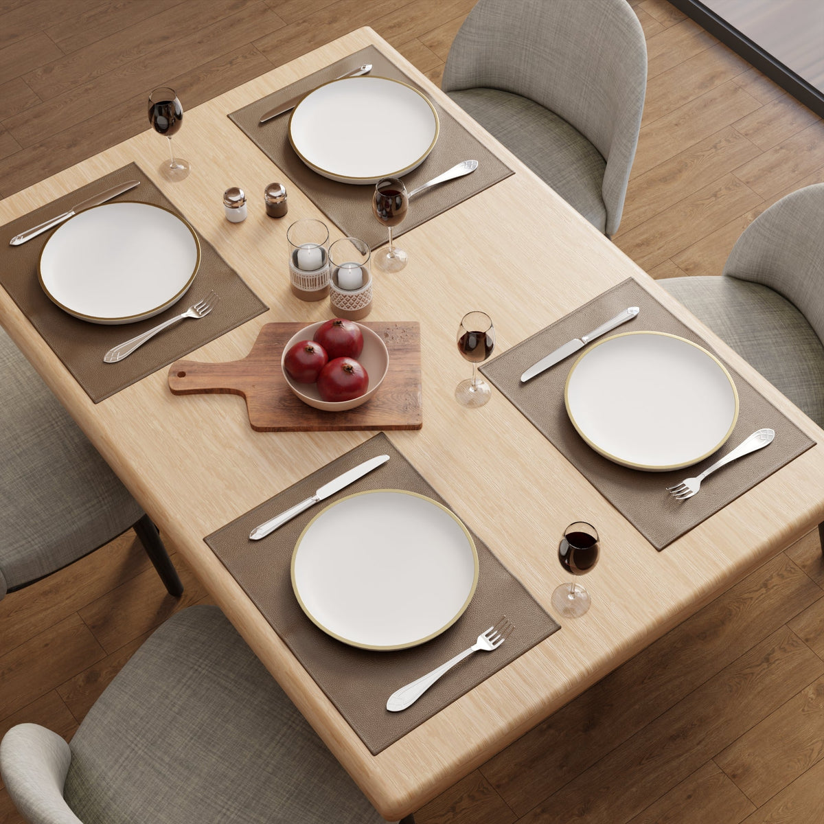 Pale wood table laid with brown faux leather placemats, gold-rimmed plates and wine glasses standing on the bare wood