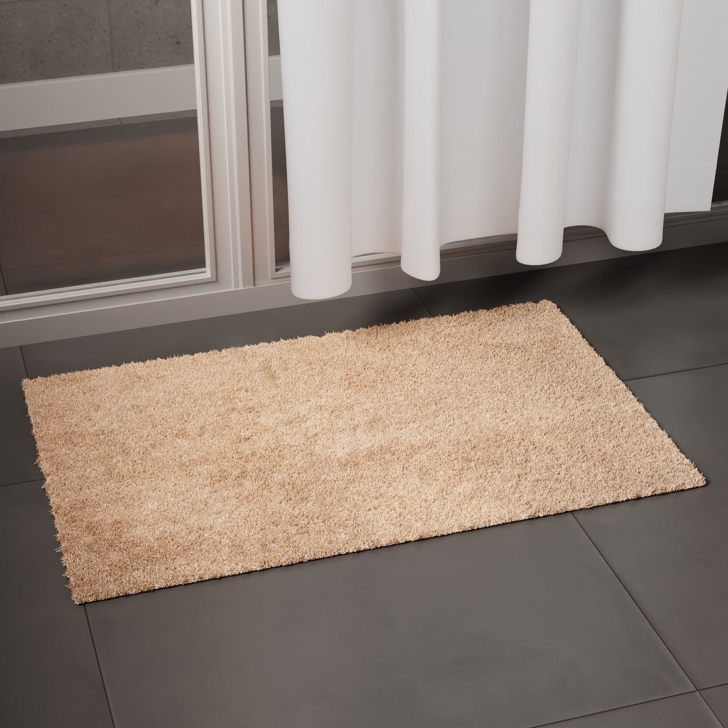 Beige cotton bathmat on a dark tiled bathroom floor beside a shower curtain